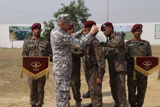 A senior officer placing maroon berets on special forces soldiers standing beside ceremonial pennants
