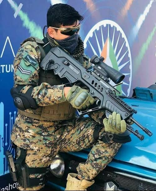 A commando in digital camouflage and body armour seated with a rifle fitted with a scope